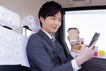 タクシーの後部座席に座りコーヒーを飲むビジネスマン
