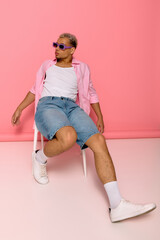 Young man showcases trendy fashion against vibrant pink backdrop in stylish pose