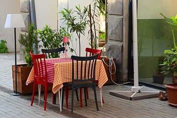 A sidewalk table outside a cafe covered with a red checkered tablecloth and wooden Viennese chairs