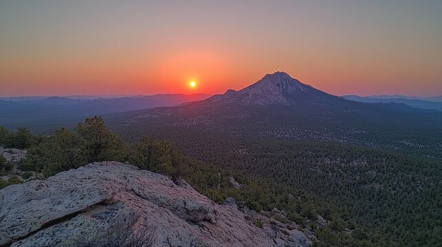 Sunrise over a mountain range. Vast panorama of a mountain peak at sunrise, with a rocky summit and forested slopes below. Warm hues of sunset paint the sky. Rocky outcrop in foreground - Powered by Adobe