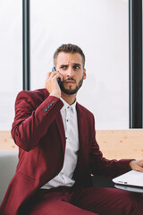 Confused worker calling on cellphone using laptop at office space