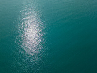Aerial view of calm turquoise sea with shimmering sunlight reflections on the surface. Peaceful and abstract natural background