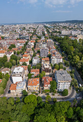 Aerial panoramic view of Varna, Bulgaria, showcasing the urban landscape with red rooftops, green parks, and the Black Sea in the distance under a clear blue sky