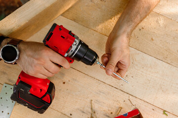 man holding a red professional drill and a self-tapping screw for wood in his hands. hands with...