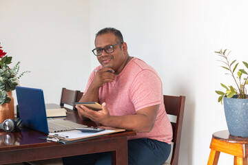A man in a red shirt sits at a table with a laptop and tablet