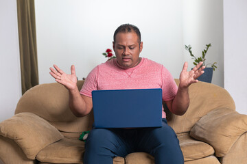A man is sitting on a couch with a laptop in front of him