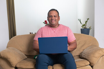 A man is sitting on a couch with a laptop in his lap