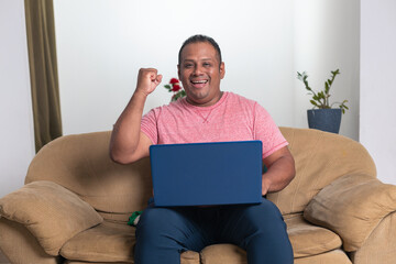A man is sitting on a couch with a laptop in front of him