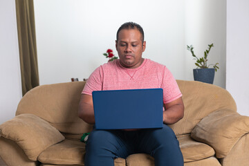 A man is sitting on a couch with a laptop in front of him