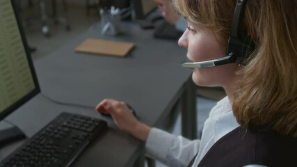 Rack focus view of positive Caucasian girl with shoulder-length hair adjusting microphone and talking with client while working in call center system on computer - Powered by Adobe