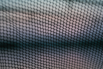 Close-up abstract view of a black mesh fabric or netting with a soft, out-of-focus background.
