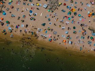 Aerial drone top down view of a crowded beach with colorful umbrellas and sunbathers during a summer afternoon near the coast