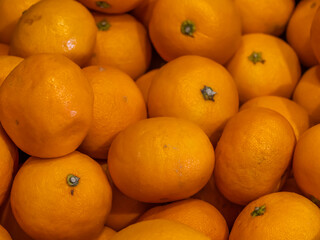 A pile of fresh, ripe tangerines with bright orange peel, displayed closely together, ready for...