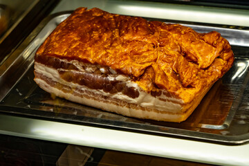 Close-up of traditional smoked pork belly with crispy rind and layered fat, displayed in a delicatessen meat counter