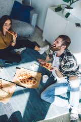Satisfied friends enjoying pizza while relaxing on floor at home