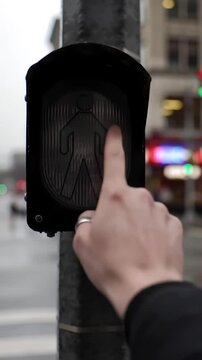 Activating the Crosswalk: A hand pushes the pedestrian signal button, illuminating the traffic lights for safe street crossing in the urban environment.