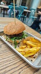 Close-up of a juicy burger with fresh greens and a side of fries served on a metal tray at an outdoor cafe. Concept of fast food indulgence, casual dining, and street food culture