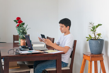 A boy is sitting at a table with a laptop and a cell phone