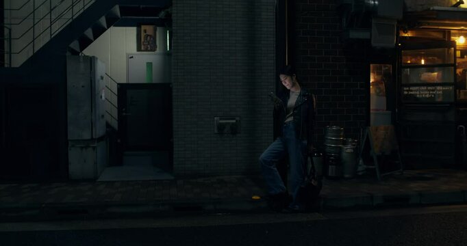 A stylish young woman smiles when using a mobile phone. She stands on a city street in Tokyo at night