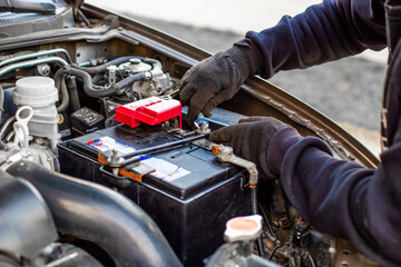 A man wearing gloves securely fastens a car battery terminal after installing it under the hood....
