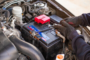 A man wearing gloves securely fastens a car battery terminal after installing it under the hood....