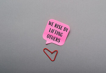 Pink and red sign that says We rise by lifting others is placed on a grey su