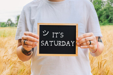 Person holding a chalkboard with the words Its Saturday written on it