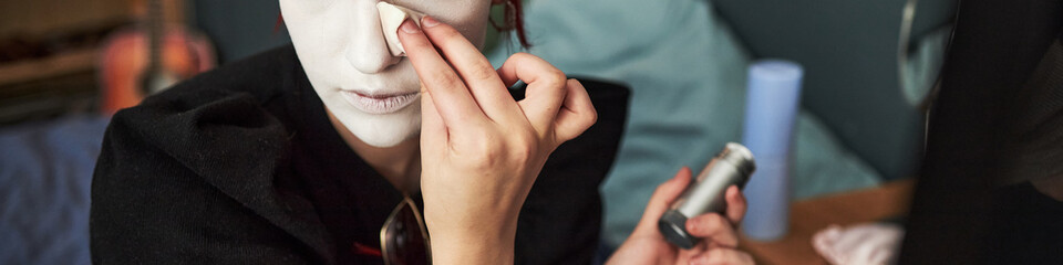 Caucasian teenage girl applying makeup to face using sponge, holding makeup stick in other hand,...