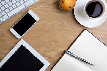 Wooden desk with modern gadgets, coffee, and a delicious muffin provides a work from home or office creative workspace