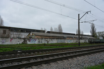 Railway track, metal lines of the railway with gray gears, green grass, large trees against the blue sky.