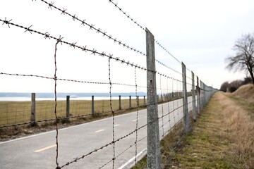 Barbed wire fence runs alongside a road, lake in the background