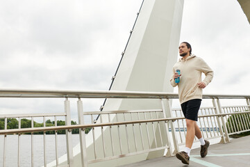 Young man in a hoodie jogging along a bridge with determination on an overcast day