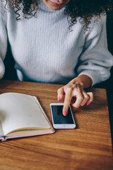 Female writing in notebook while text messaging on smartphone