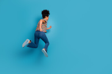 Young woman in striped t-shirt jumping energetically against a turquoise background, embodying a...