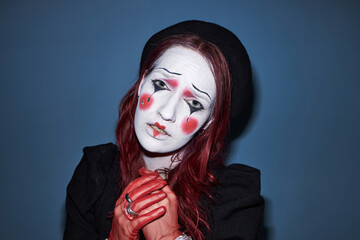 Portrait of Caucasian young adult woman with mime makeup and red painted hands posing with sad...