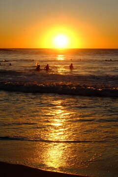 Golden sunrise over the ocean with silhouettes of people in the water