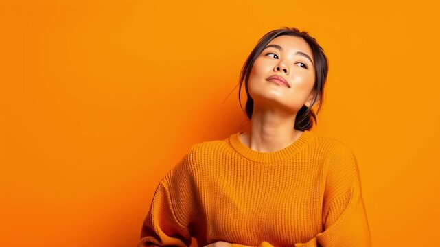 Thoughtful young woman looking up at empty thought bubbles on a bright orange background, suggesting imagination and decision-making. Concept of creativity, ideas and contemplation
