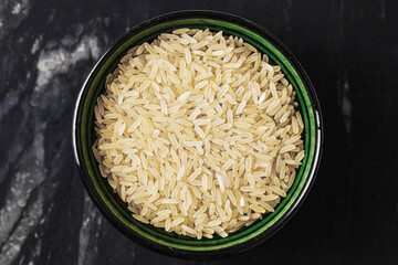Bowl of uncooked brown rice. Raw grains in ceramic container. Simple healthy food. Ingredient for...