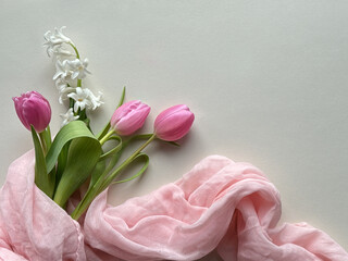 Pink tulips and white hyacinth flowers arranged with soft pink fabric on a light background