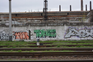 Railway track, metal lines of the railway with gray gears, green grass, large trees against the blue sky.