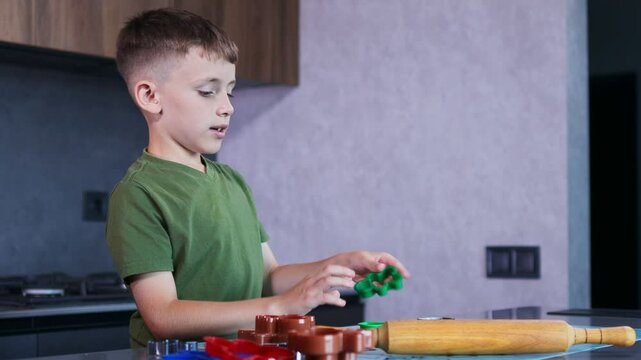 Little boy making cookies using cookie cutters and dough in the kitchen at home.