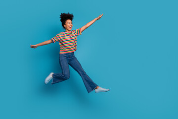 Cheerful young woman in striped t-shirt jumping with joy against turquoise background showcasing...