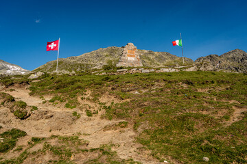 Mountain Border Landmark on Splugen Pass: Swiss and Italian Flags Mark the Historic Alpine Divide...