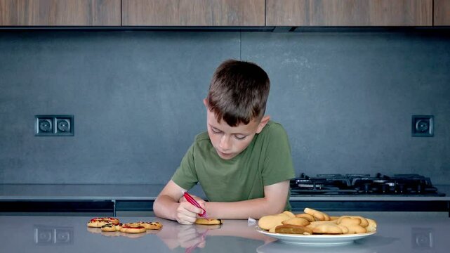 Cute boy decorating gingerbread cookies at home kitchen.