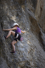 A woman is climbing a rock wall wearing a helmet and a purple tank top