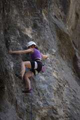 A woman is climbing a rock wall with a red and white striped backpack