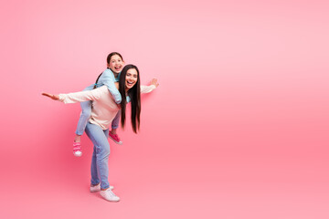 Joyful piggyback ride with mother and daughter against vibrant pink backdrop showcasing family bonding and happiness.