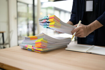 A man is holding a stack of papers on a desk. The papers are yellow, pink, and green, and they are...
