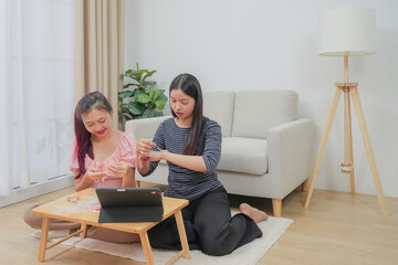 Two young asian women stringing beads on thread and choosing colorful beads from box to making handmade bracelet while spending time to creating jewelry handicraft and doing hobby lifestyle at home. 