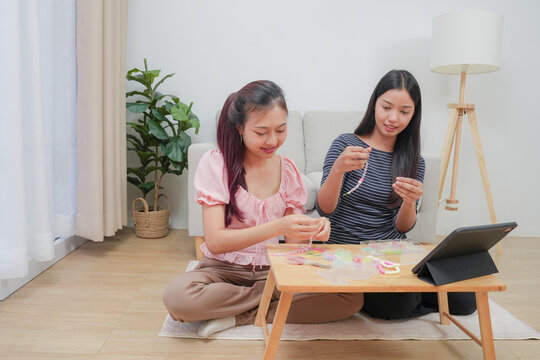 Two young asian women stringing beads on thread and choosing colorful beads from box to making handmade bracelet while spending time to creating jewelry handicraft and doing hobby lifestyle at home. 